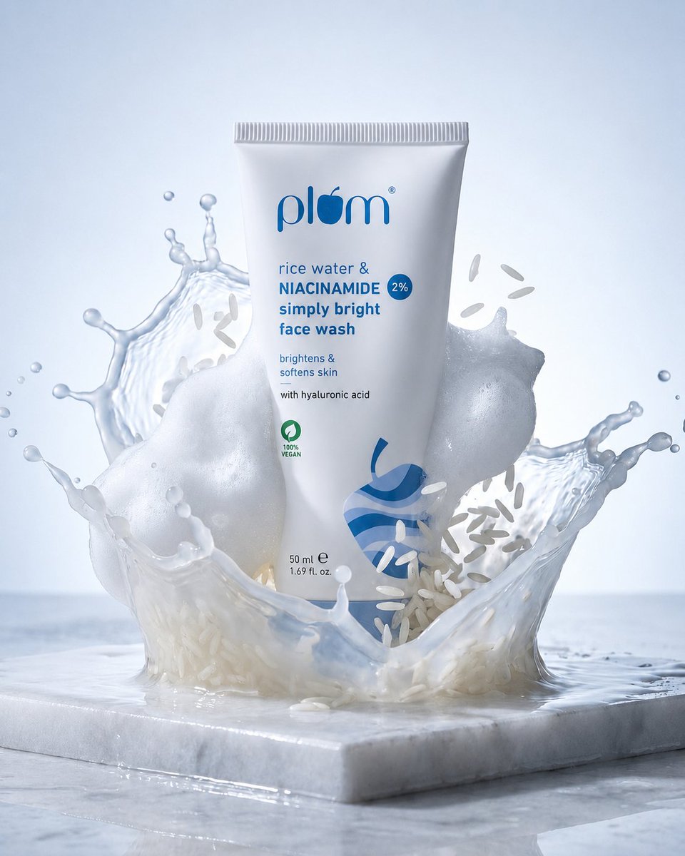 White face wash tube on marble surrounded by splash, foam, and floating rice grains.